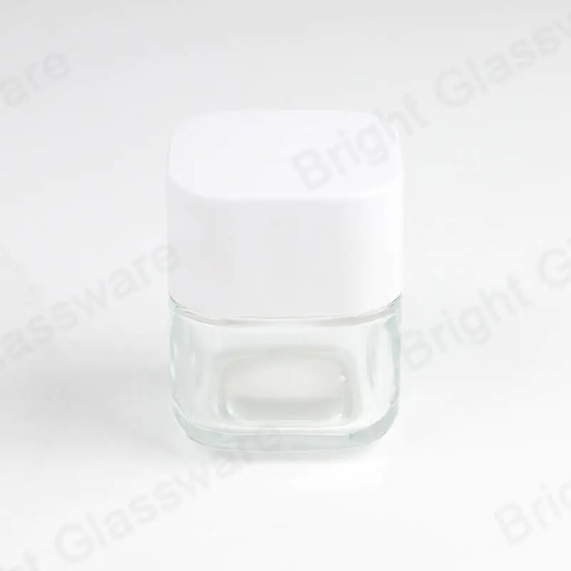 白いふた付きの透明な正方形のガラスの化粧品の瓶